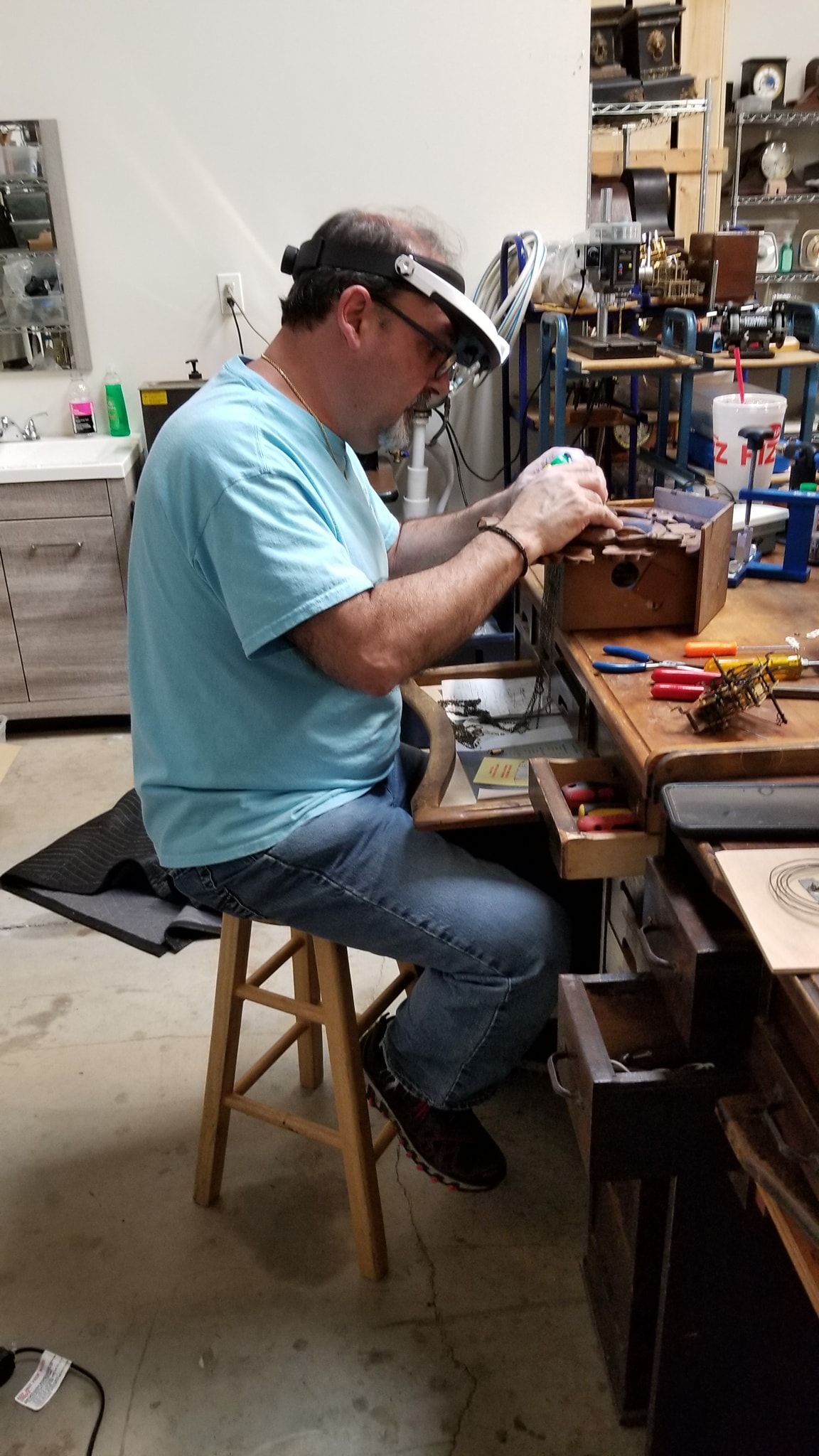 A man is sitting on a stool in a workshop working on a piece of jewelry.