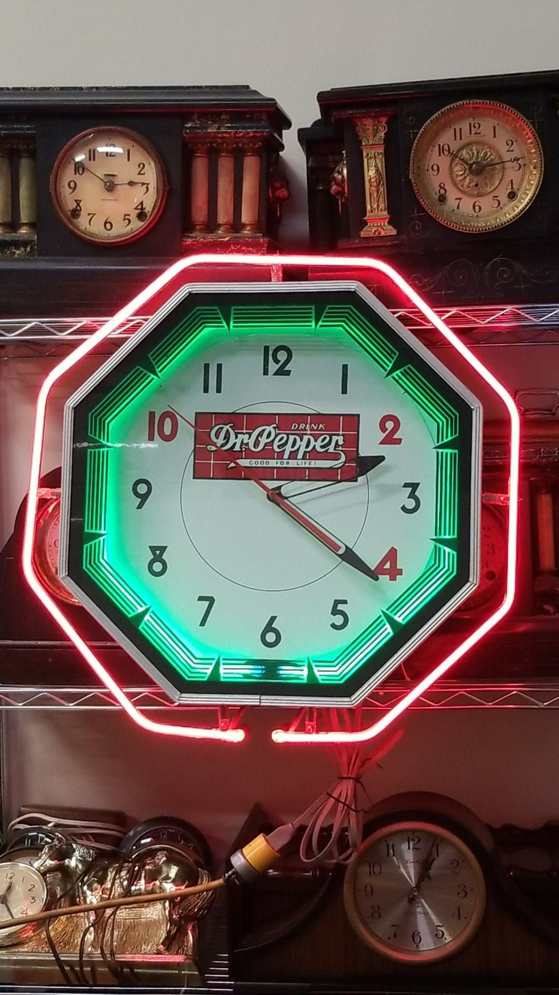 A neon clock is hanging on a wall next to other clocks.