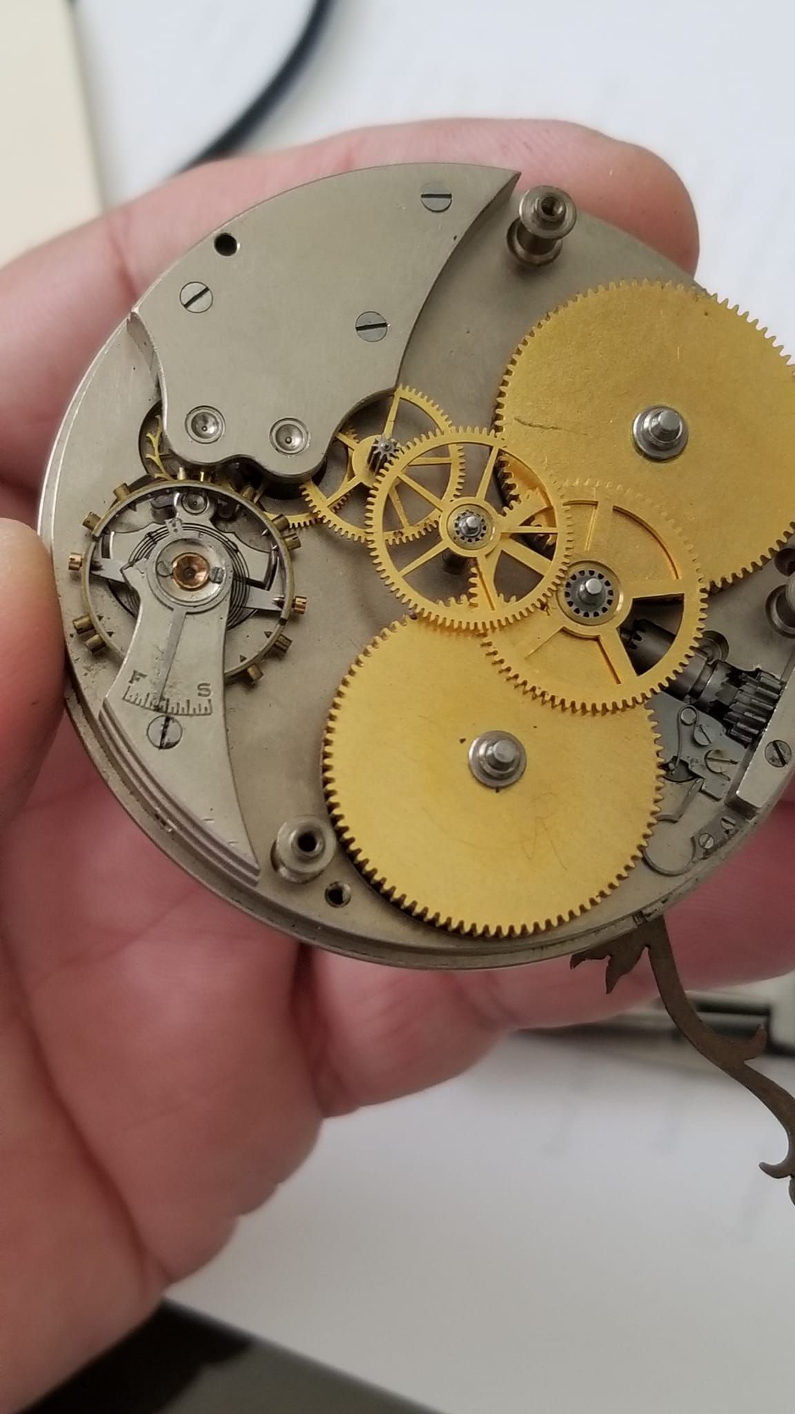 A person is holding a watch mechanism in their hand.