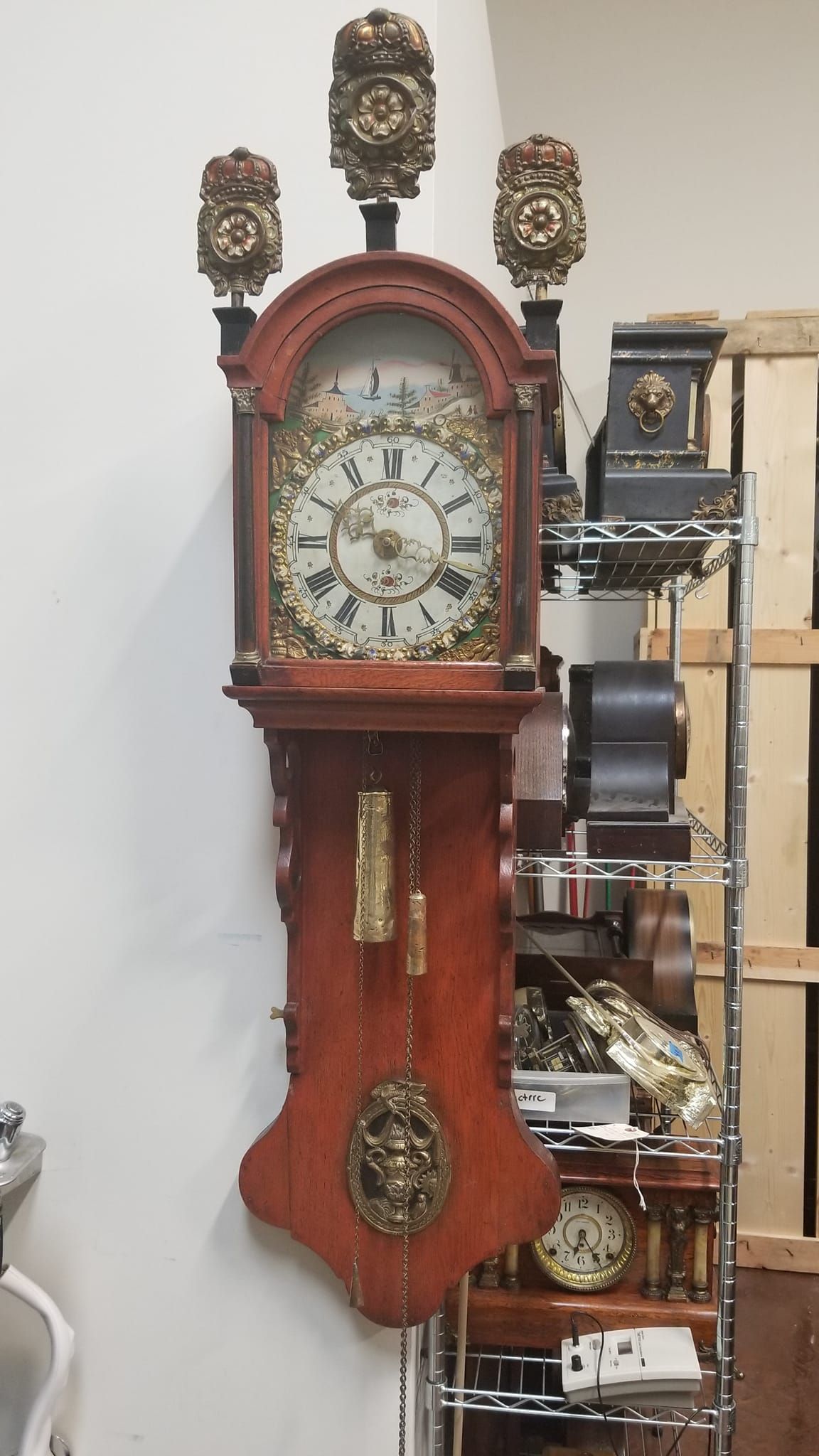 A large clock is hanging on a wall next to a rack of clocks.