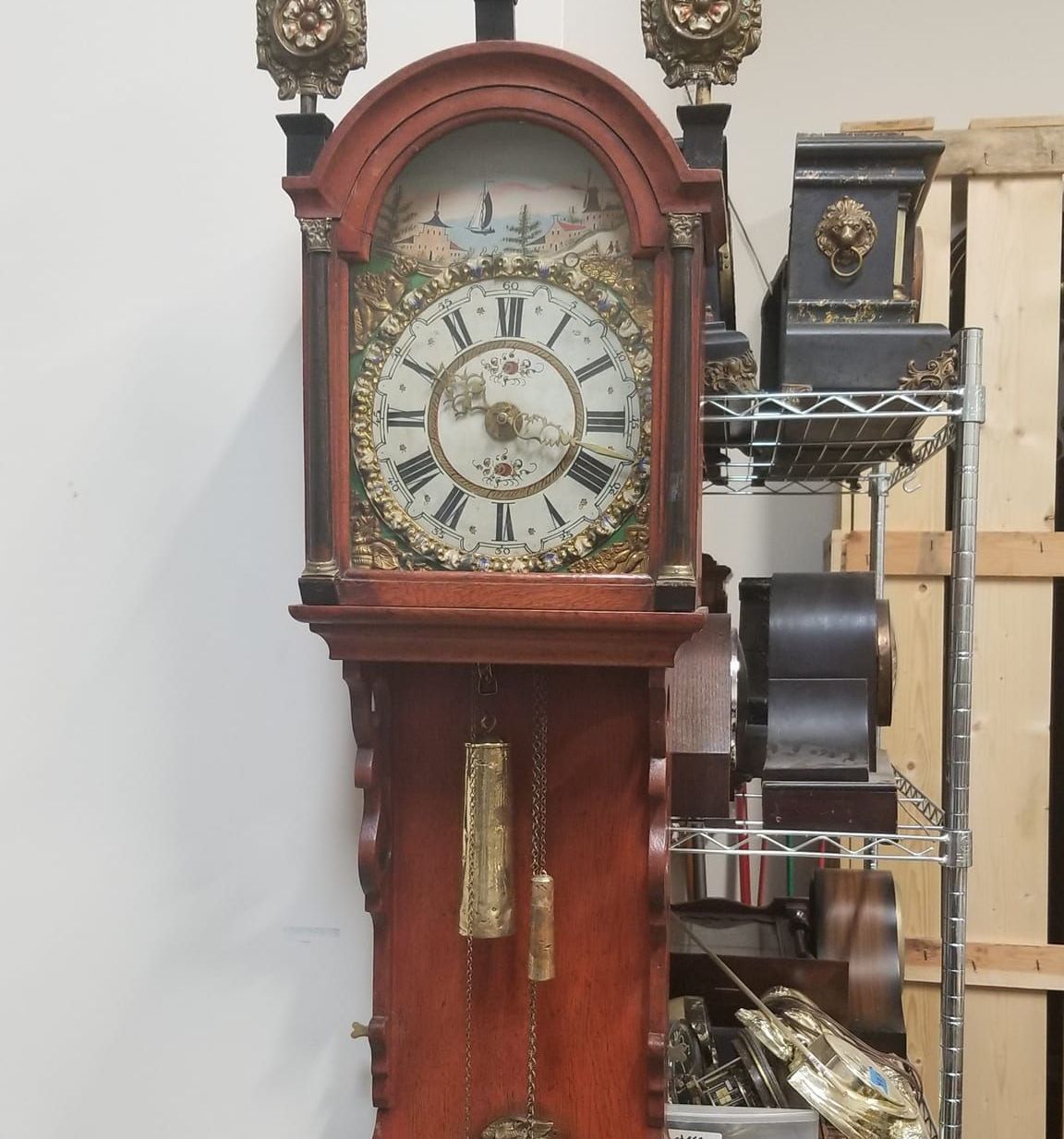 A large clock is hanging on a wall next to a rack of clocks.