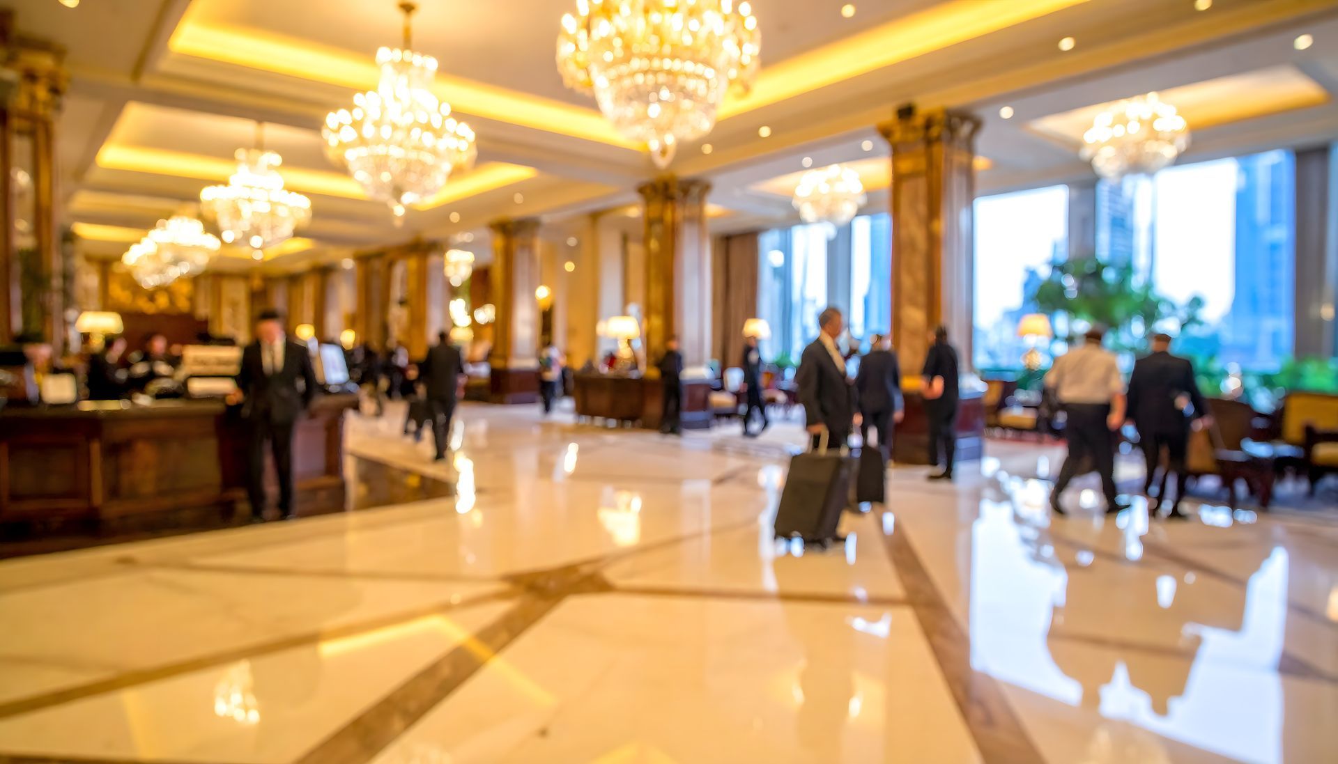 Grand hotel lobby with chandeliers, guests, reception desk, and luggage.