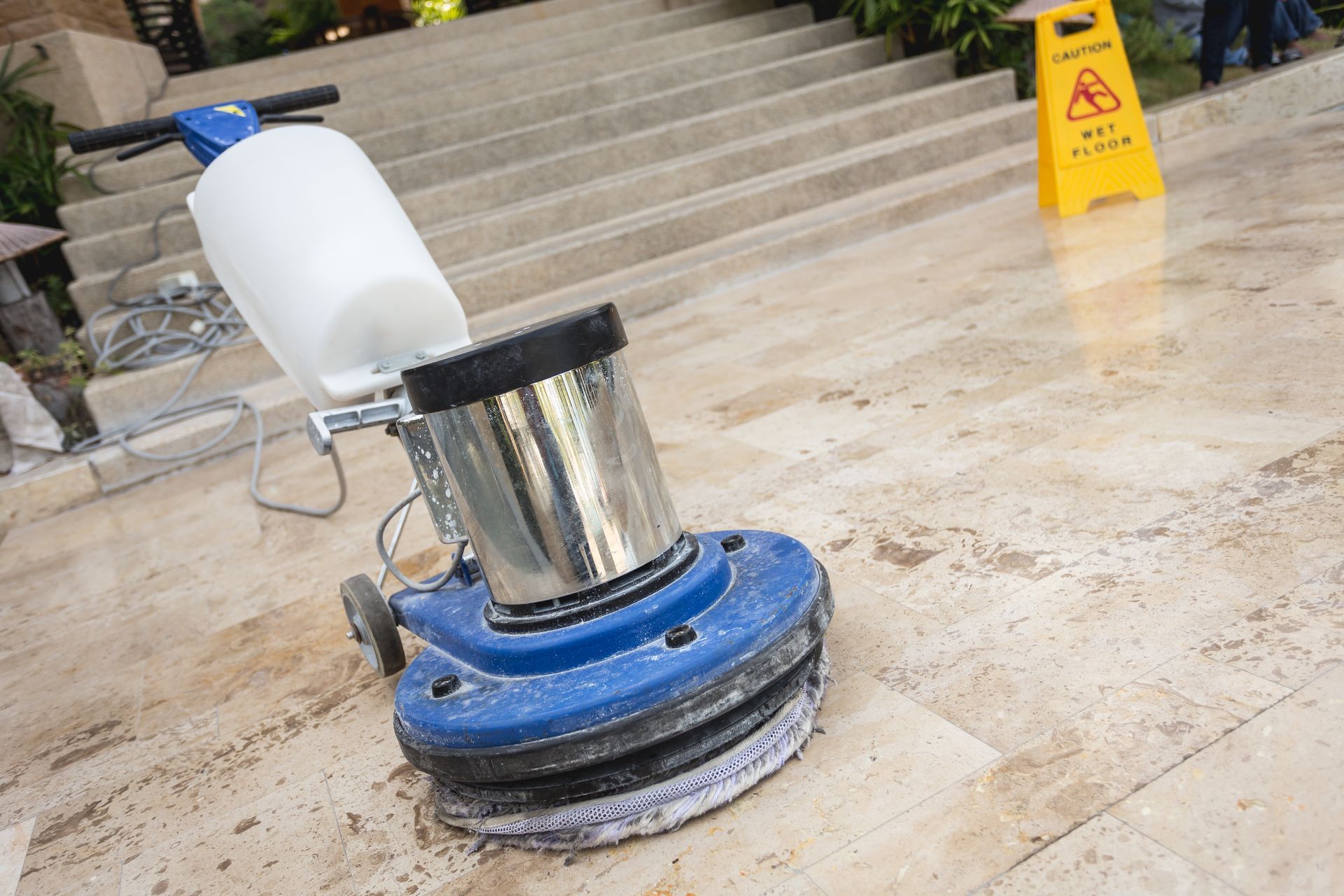 Person sanding a dark surface with a power sander; dust particles visible; hands wearing yellow gloves.