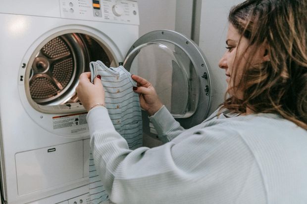 A woman is putting clothes in a washing machine.