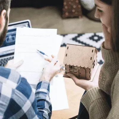 A man and a woman are sitting at a table looking at papers and a model house.
