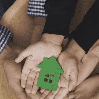 A group of people are holding a green house in their hands.
