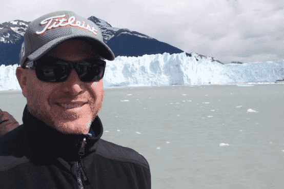 A man wearing a hat and sunglasses is standing in front of a glacier.