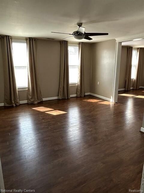 An empty living room with hardwood floors and a ceiling fan.