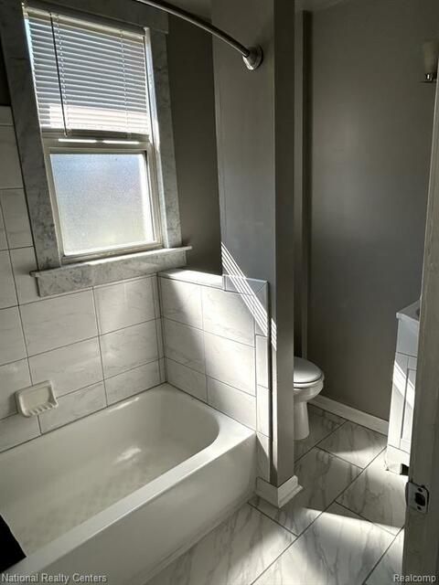 A bathroom with a tub , toilet and window.