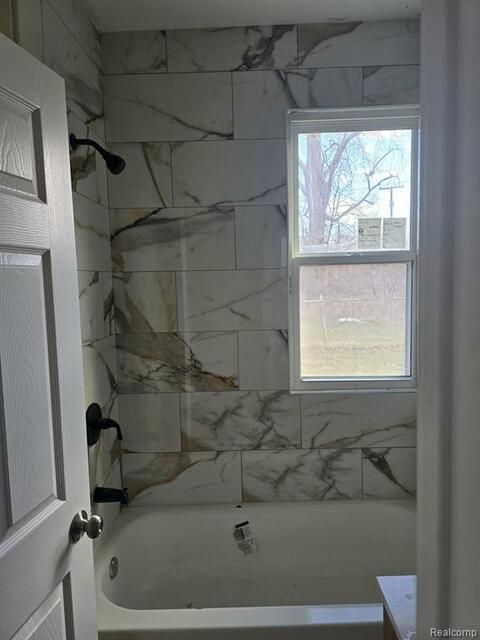 A bathroom with a tub , shower , and window.