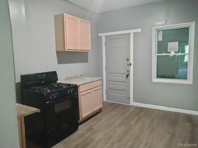 A kitchen with a stove , sink , cabinets and a window.
