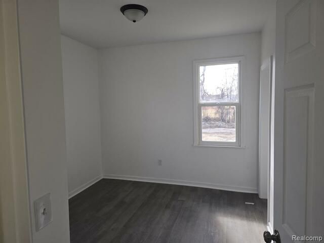 An empty bedroom with a window and hardwood floors.