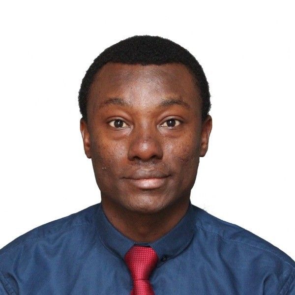 Man with dark skin in a blue shirt and red tie, looking at the camera.