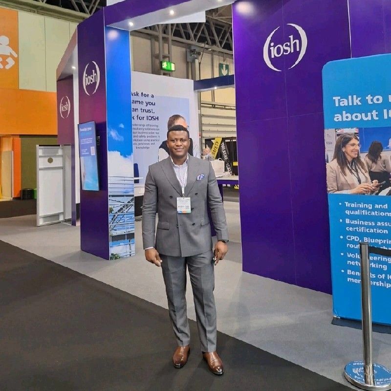 Man in grey suit stands near an IOSH booth at a conference. Purple and white signage in the background.