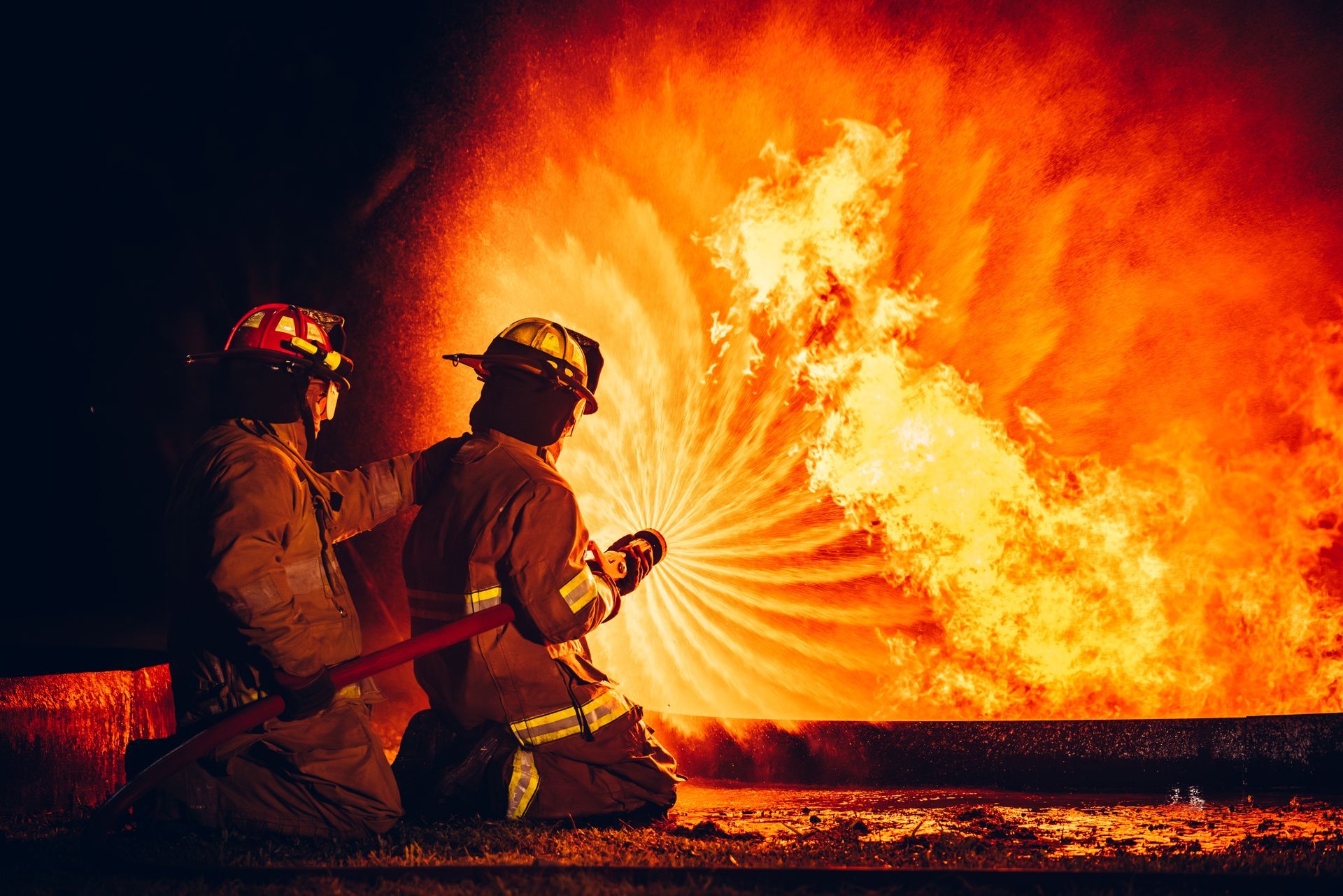 Firefighters battling a massive fire with a hose, flames erupting.