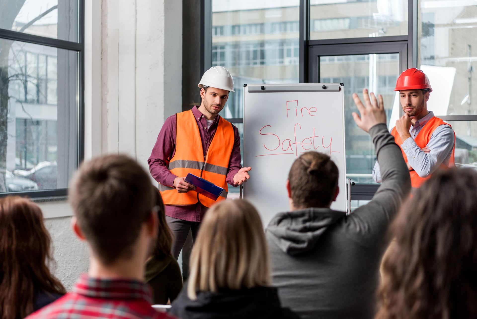 Construction workers lead a fire safety training with a raised hand for a question.