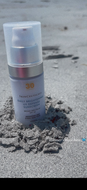 A bottle of sunscreen is sitting on a pile of rocks on the beach.