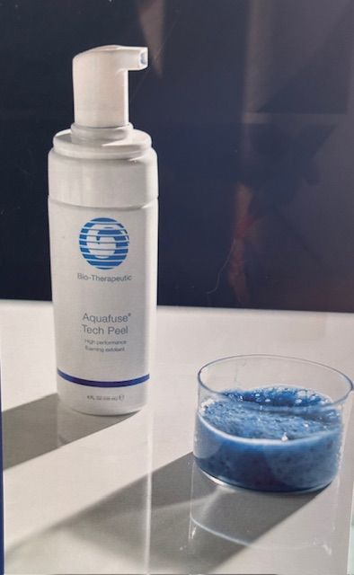 A bottle of foaming soap next to a glass of blue liquid