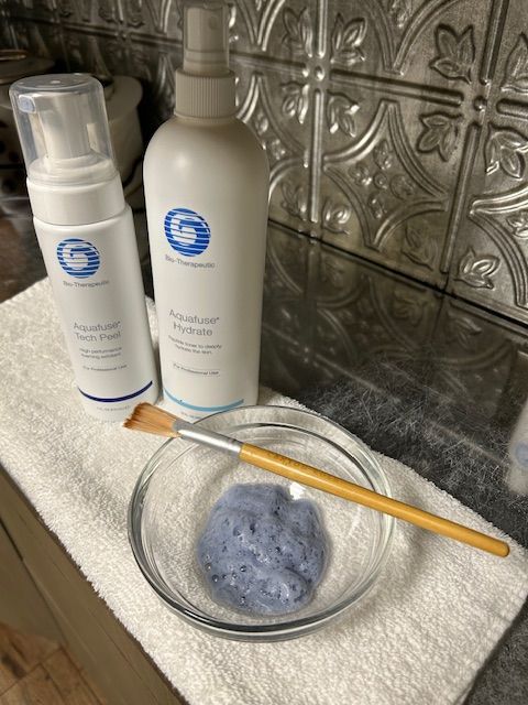 Two bottles of lotion and a bowl of powder with a brush on a towel.