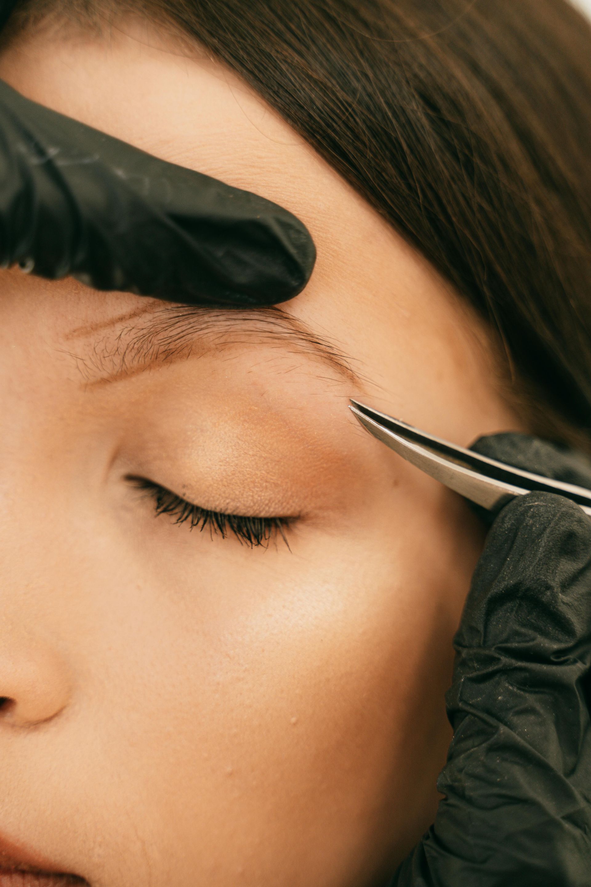 A woman is getting her eyebrows trimmed with tweezers.
