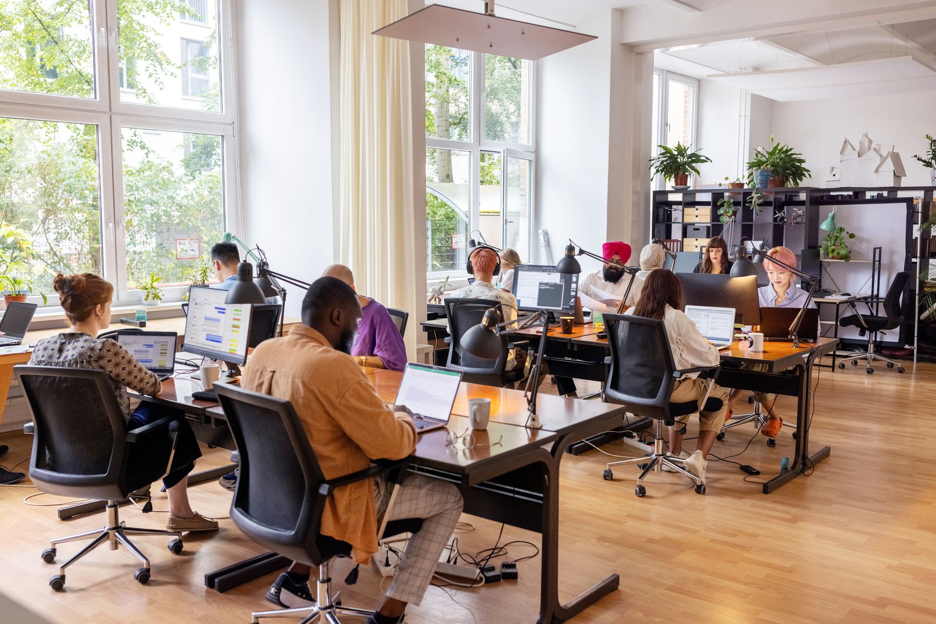 People working at desks in a bright, modern office with large windows.