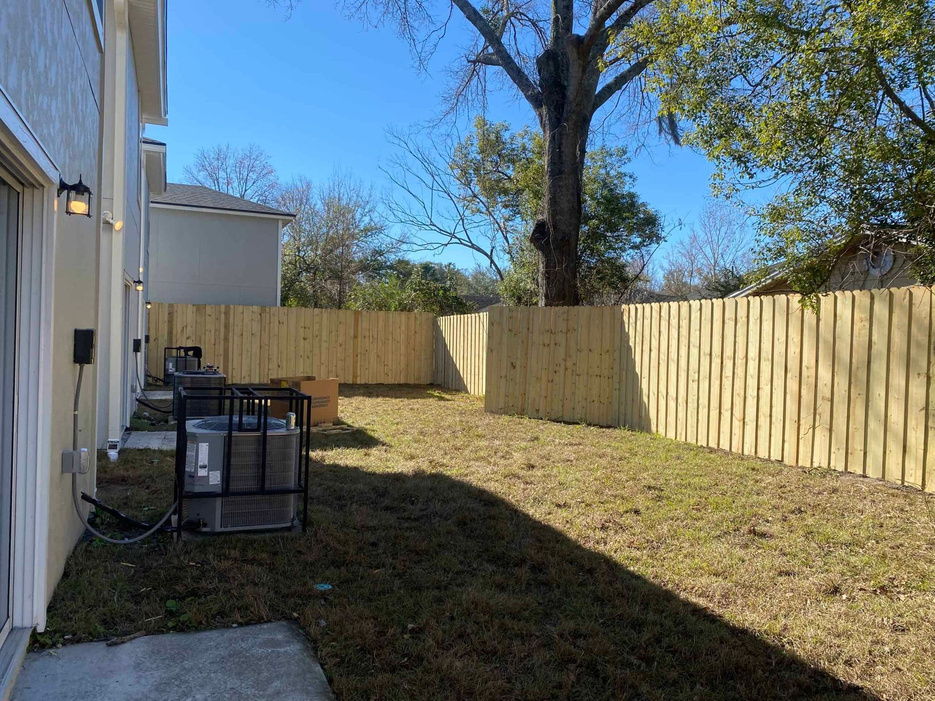 A backyard with a wooden fence and a tree in the background.