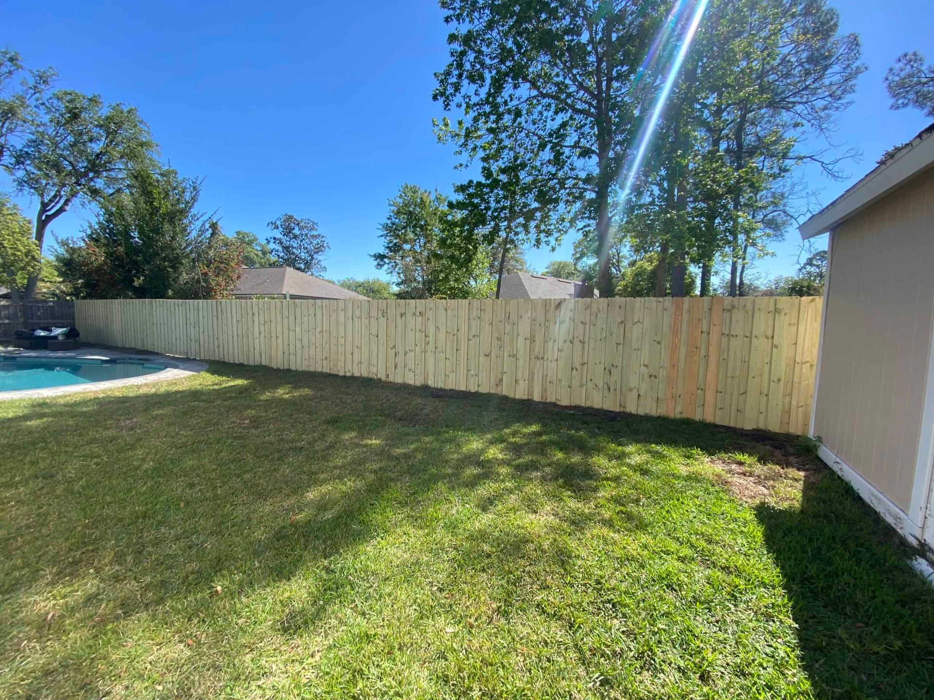 A wooden fence surrounds a swimming pool in a backyard.