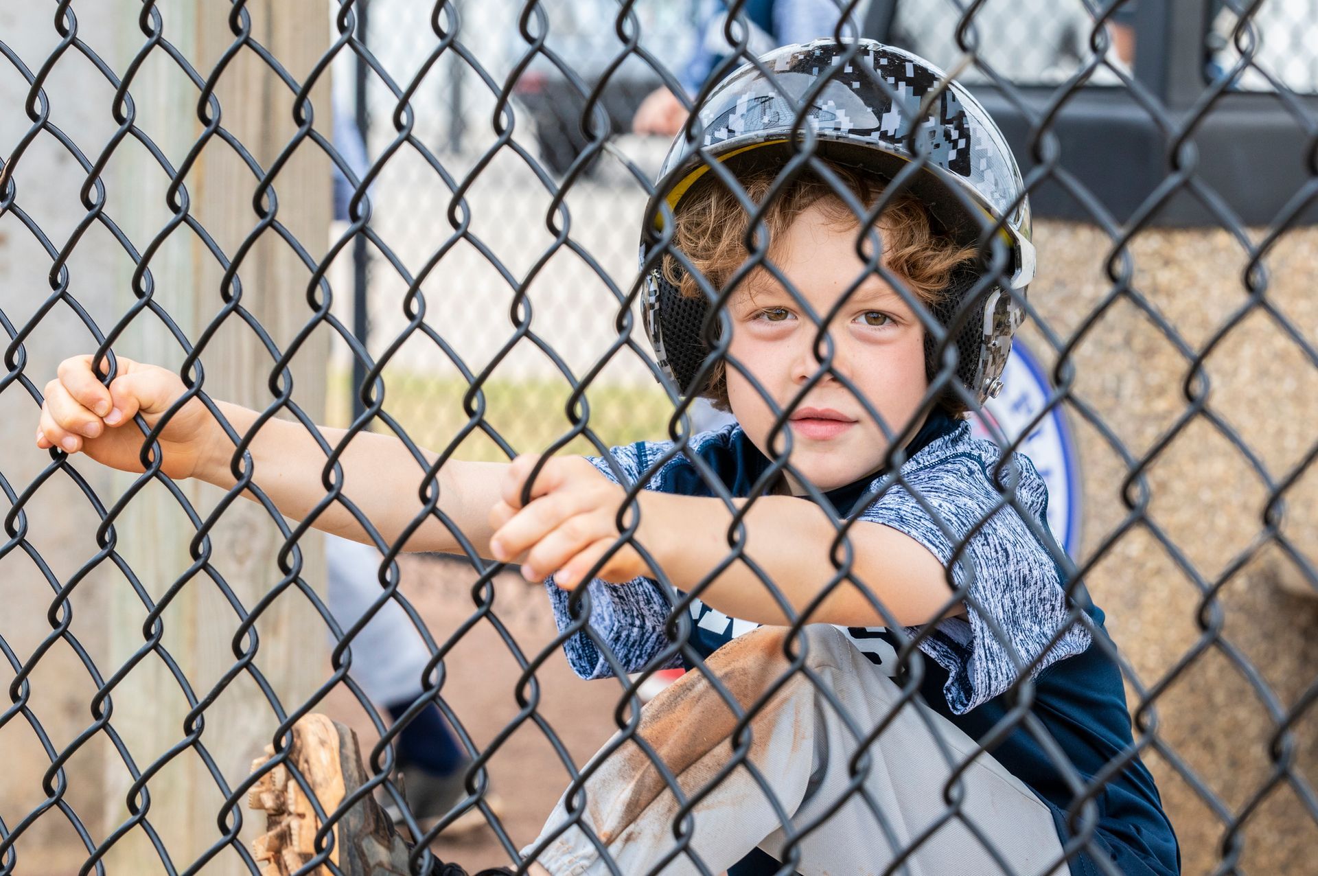 A young boy wearing a helmet is behind a chain link fence.