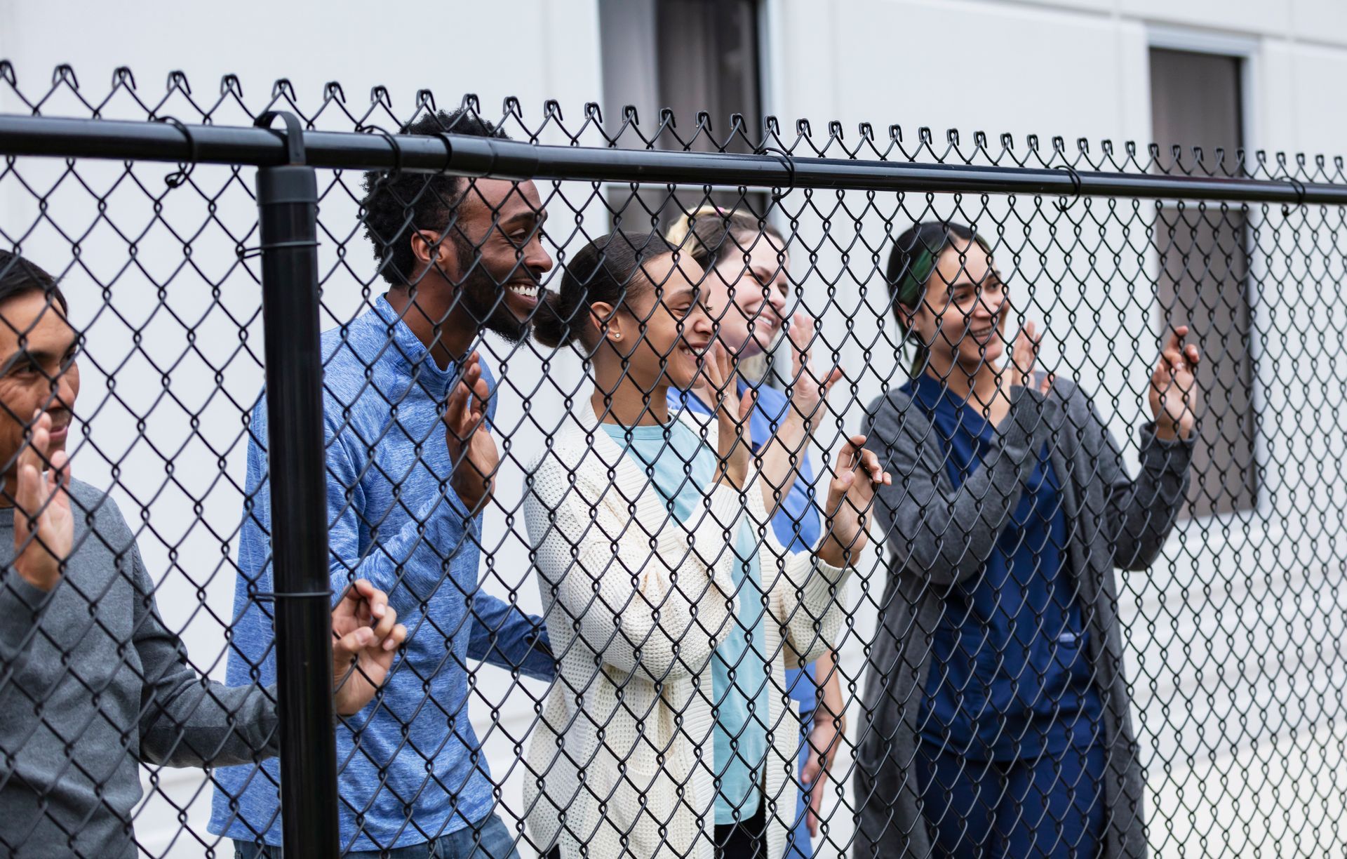 A group of people are standing behind a chain link fence.