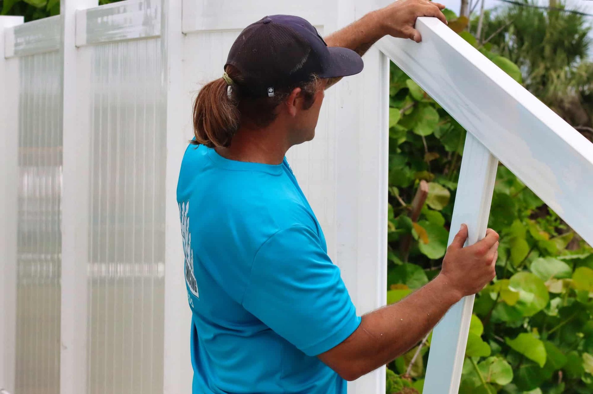 A man in a blue shirt is working on a white fence