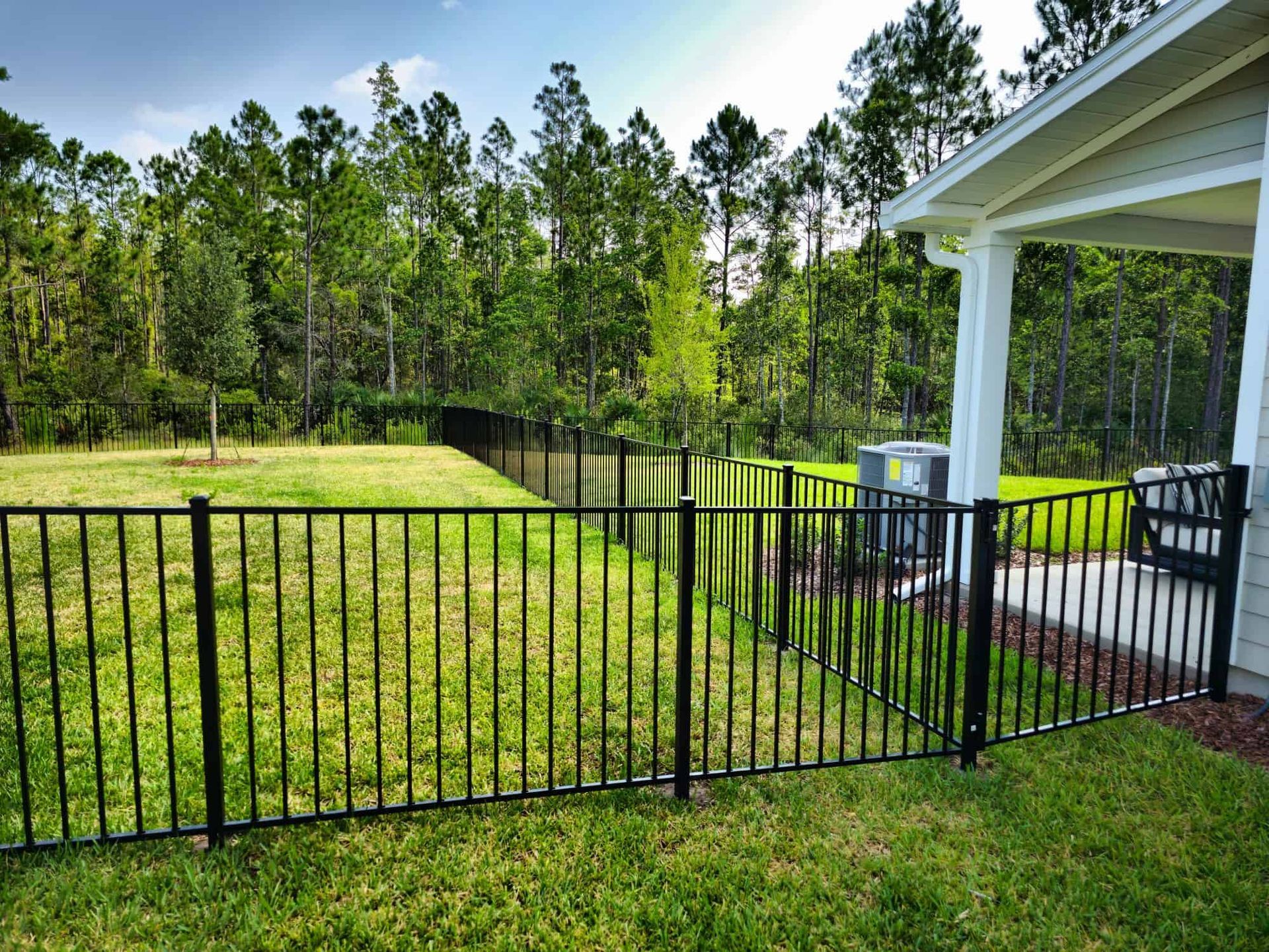 A black fence surrounds a lush green field in front of a house.