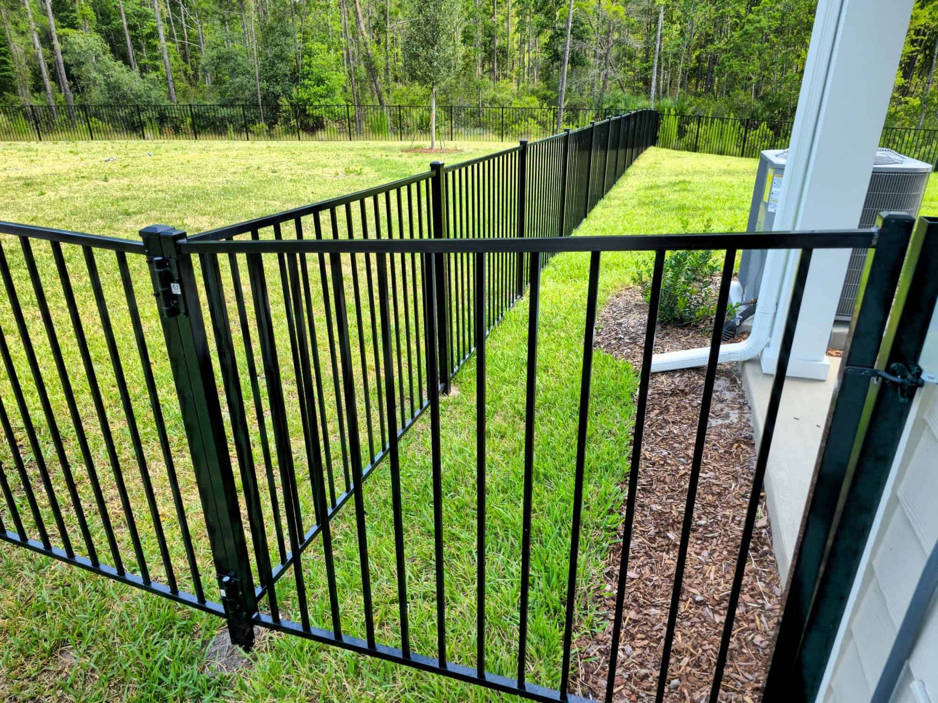 A black metal fence surrounds a lush green field.