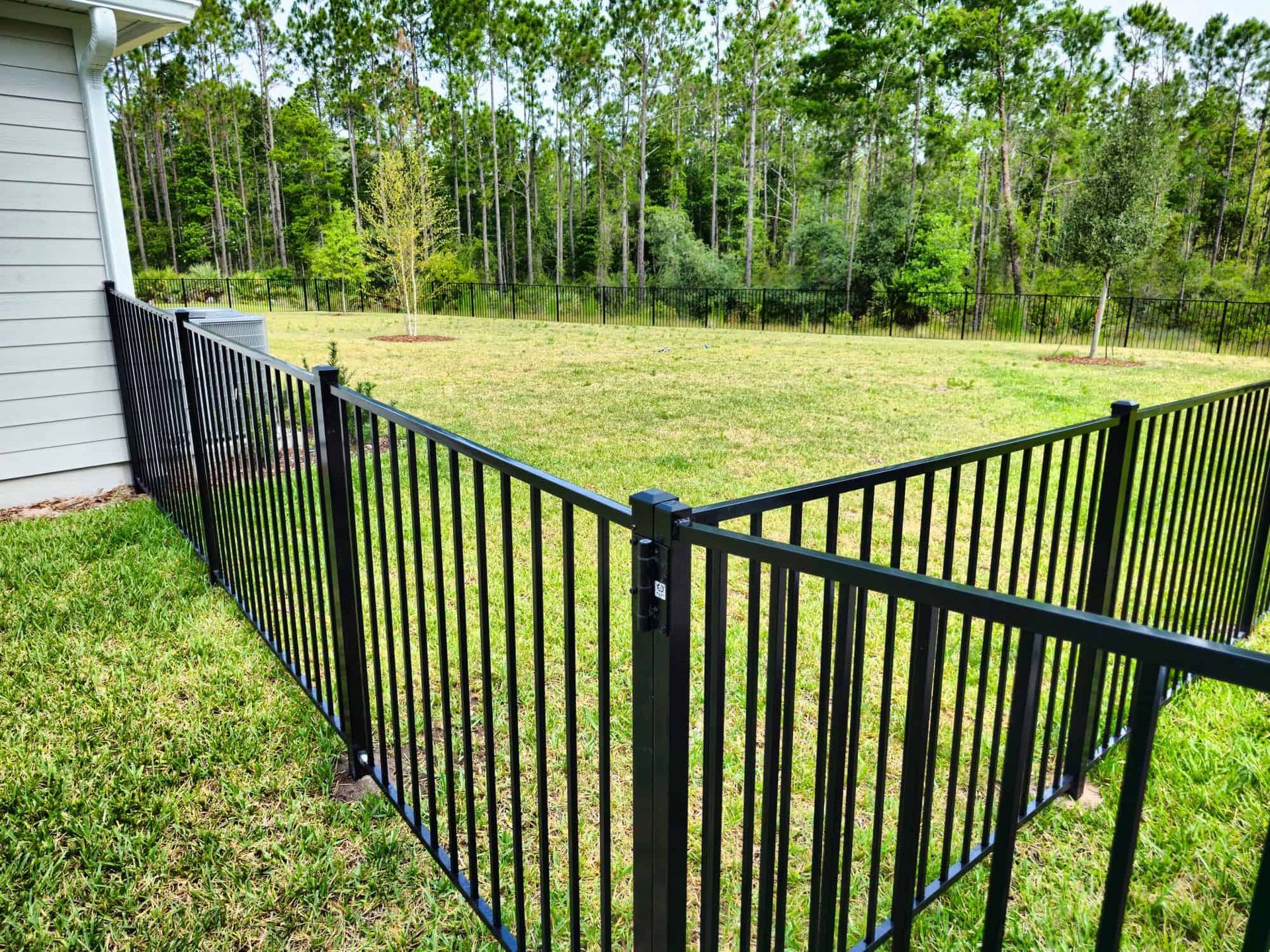 A black fence surrounds a grassy field in front of a house.