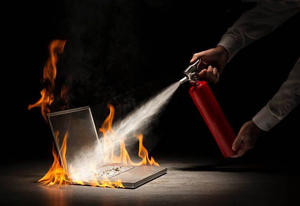 hands of man extinguishing fire on laptop