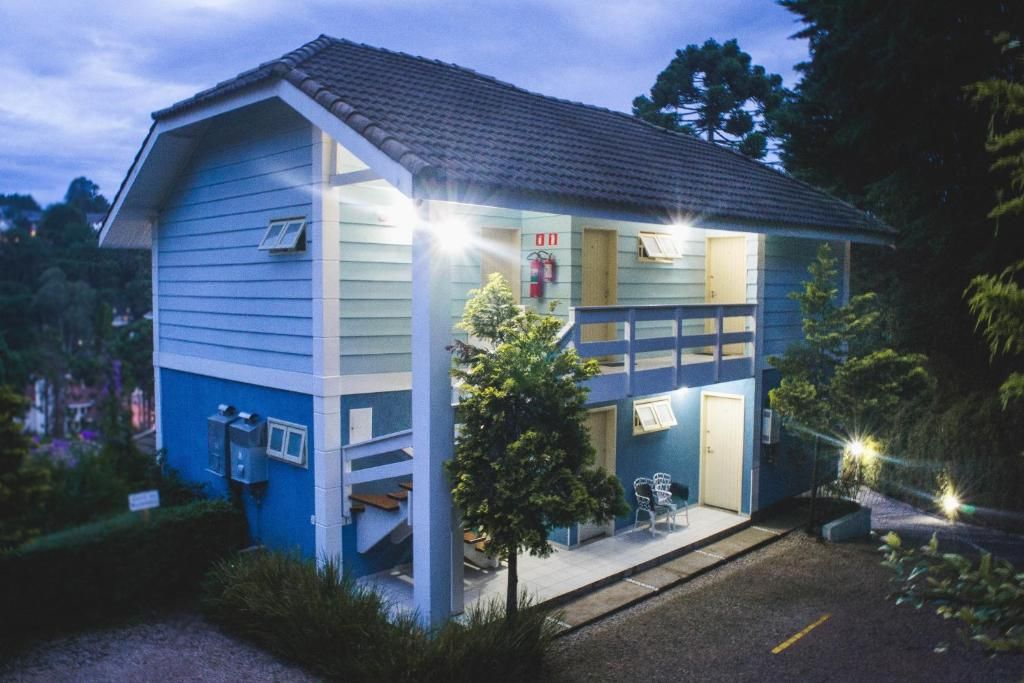 Um prédio de madeira azul de dois andares com telhado de telhas, iluminado por luzes externas ao entardecer, situado em um terreno de cascalho.