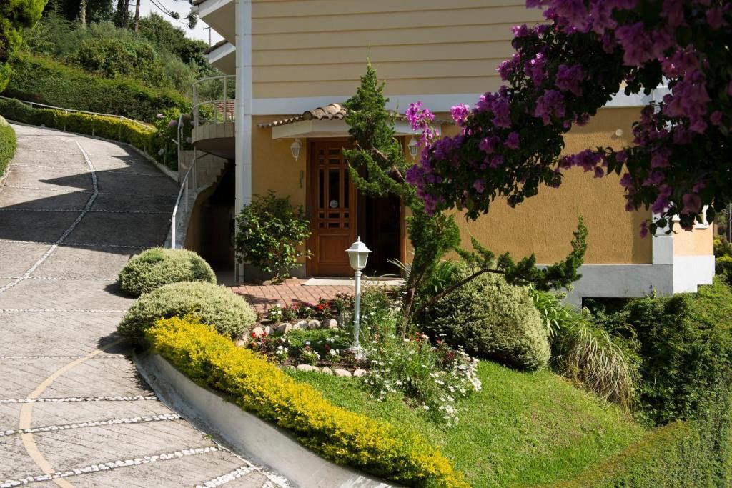 Uma casa bege com uma entrada de automóveis em pedra, um jardim frontal ajardinado e flores de buganvília roxas.