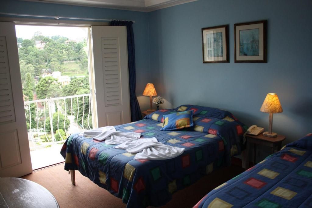 Um quarto de hotel com duas camas, paredes azuis, roupa de cama estampada, dois abajures e uma porta de varanda aberta com vista para as árvores.