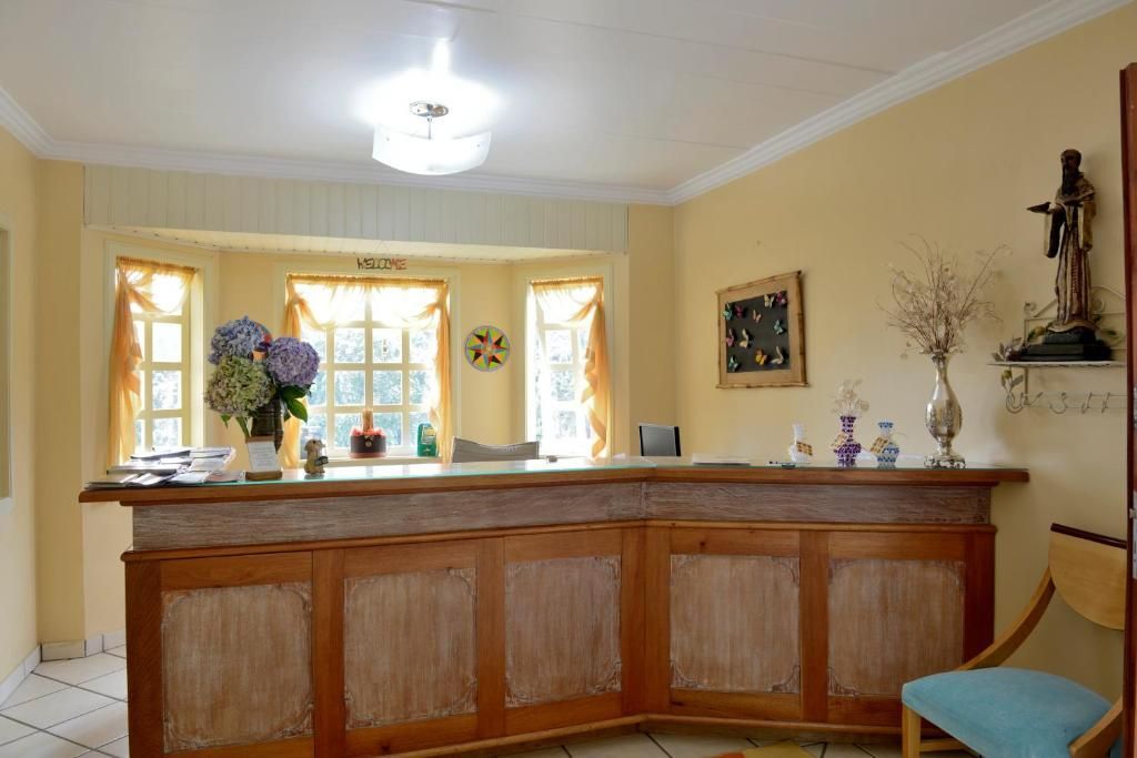 Balcão de recepção com painéis de madeira clara, paredes amarelas e uma janela saliente em um saguão de hotel ou ambiente de escritório.