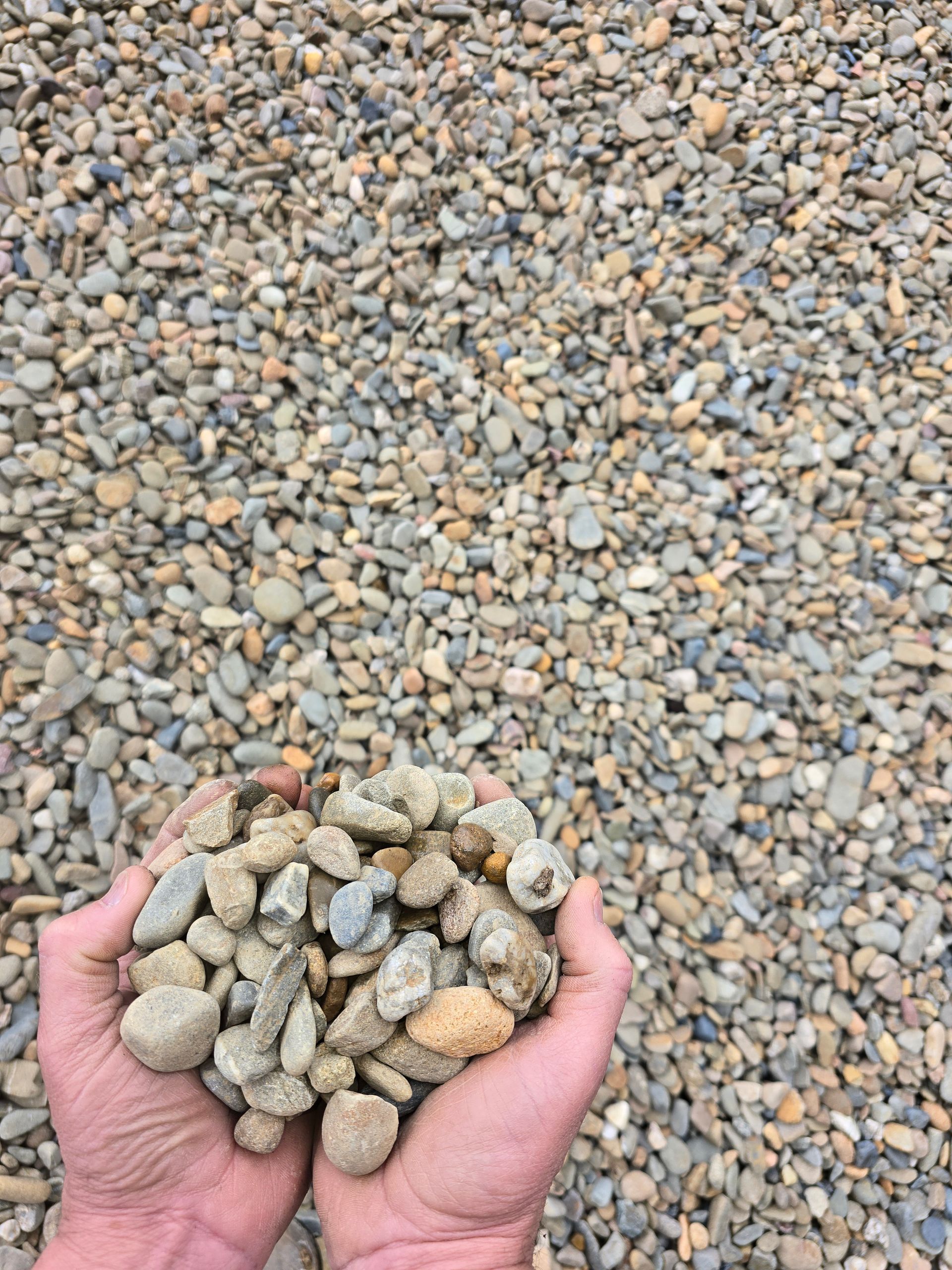 Hands Holding a Pile of Small, Rounded Gravel Stones — BVN Landscape & Steel Supplies in Nowra, NSW