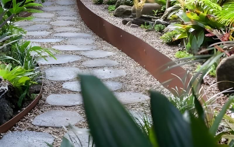 A stone stepping-stone path winds through a garden, bordered by metal edging and surrounded by lush green foliage. — BVN Landscape & Steel Supplies in St Georges Basin, NSW