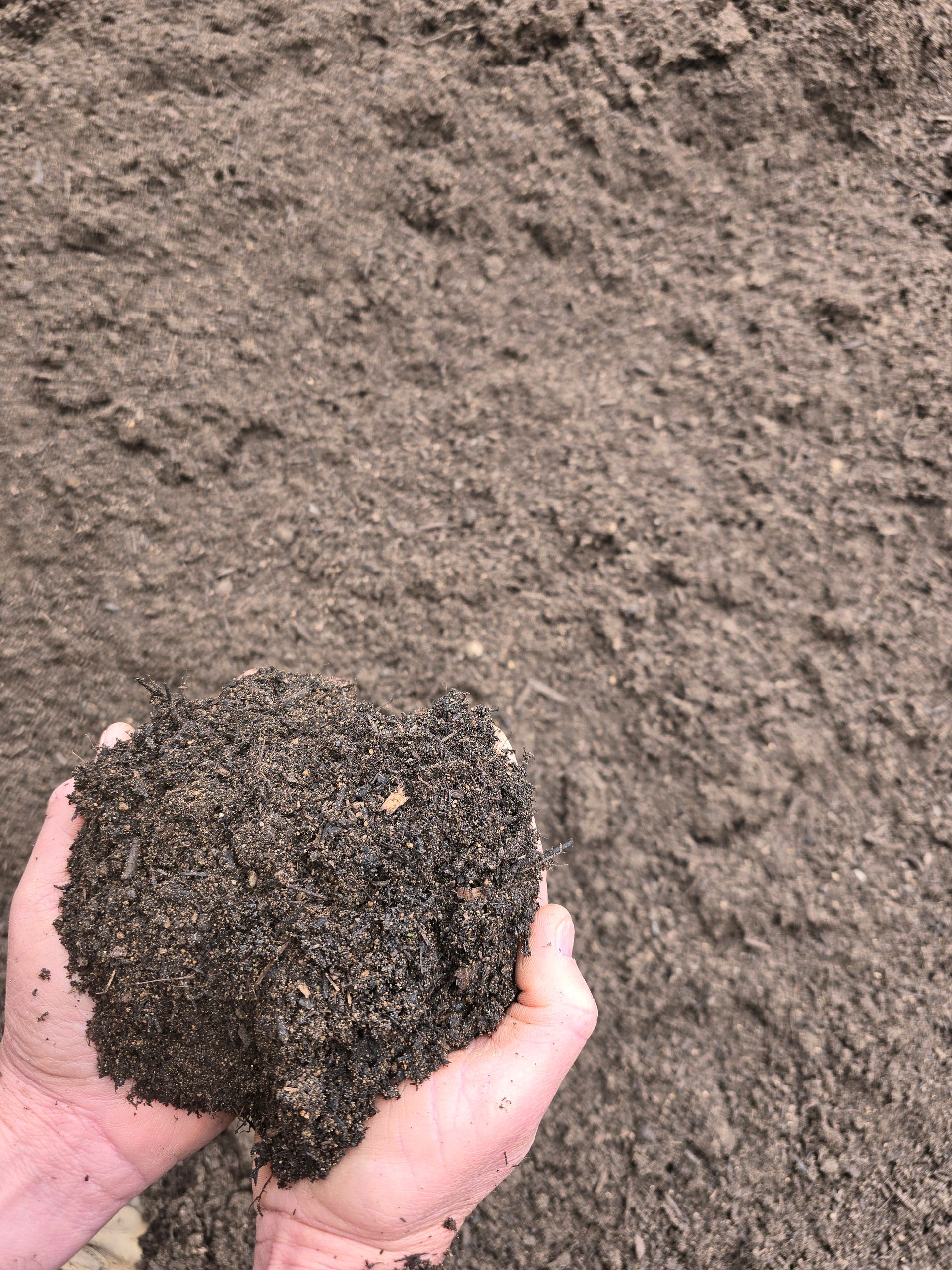 Hands Hold a Dark, Damp Clump of Soil — BVN Landscape & Steel Supplies in Vincentia, NSW
