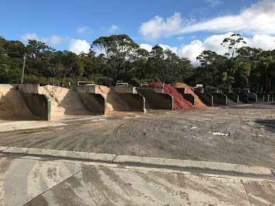 A Row of Dumpsters Are Lined up In a Dirt Field with Trees — BVN Landscape & Steel Supplies in Vincentia, NSW
