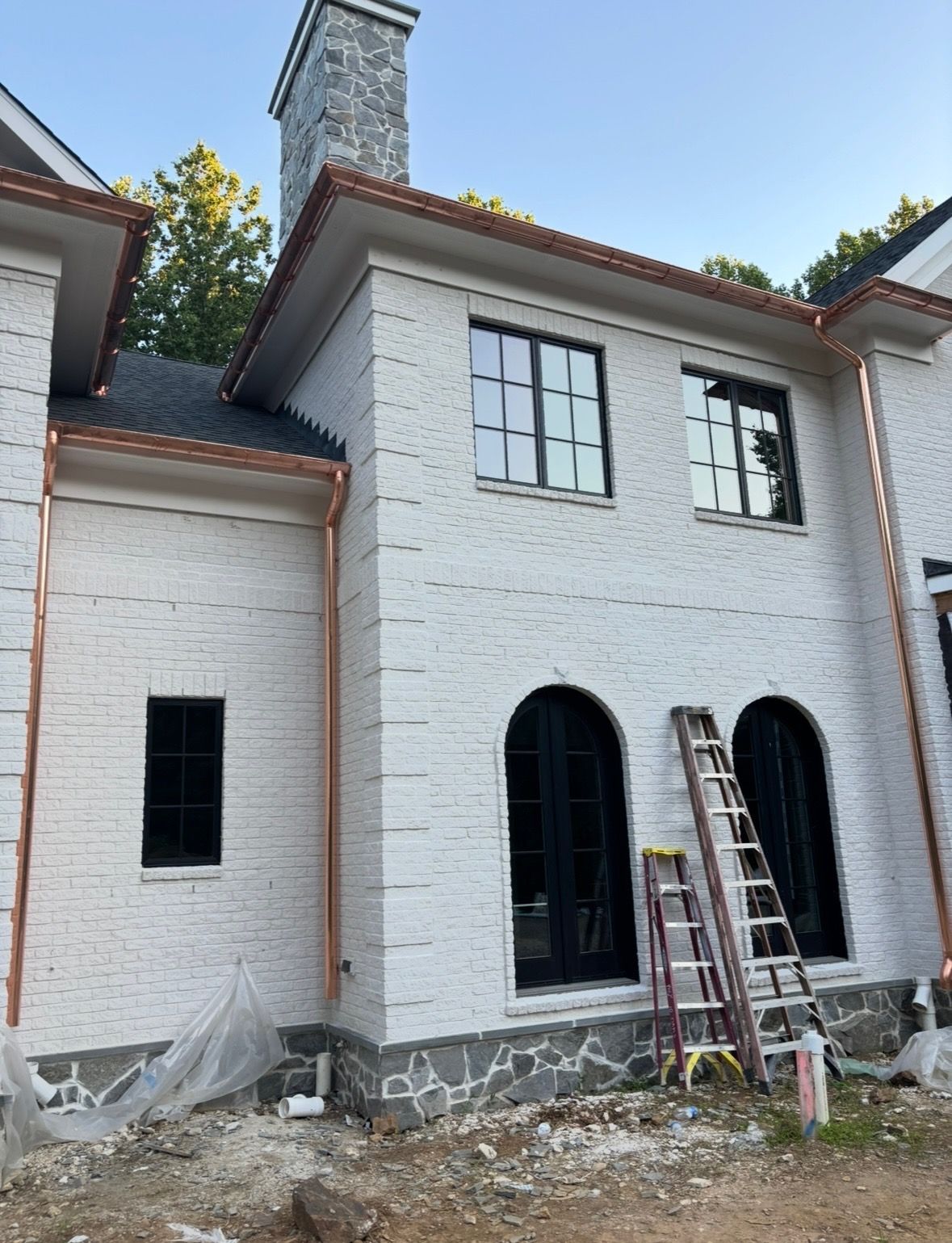 A white brick house with copper gutters and arched windows is being built.