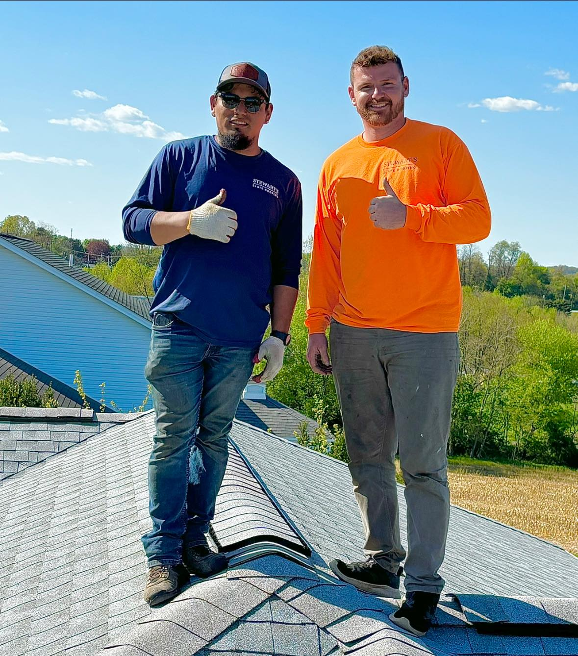 Two men are standing on top of a roof giving a thumbs up.