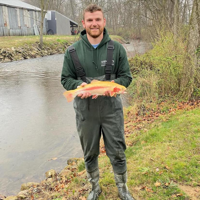A man in a green hoodie is holding a large fish in his hands.