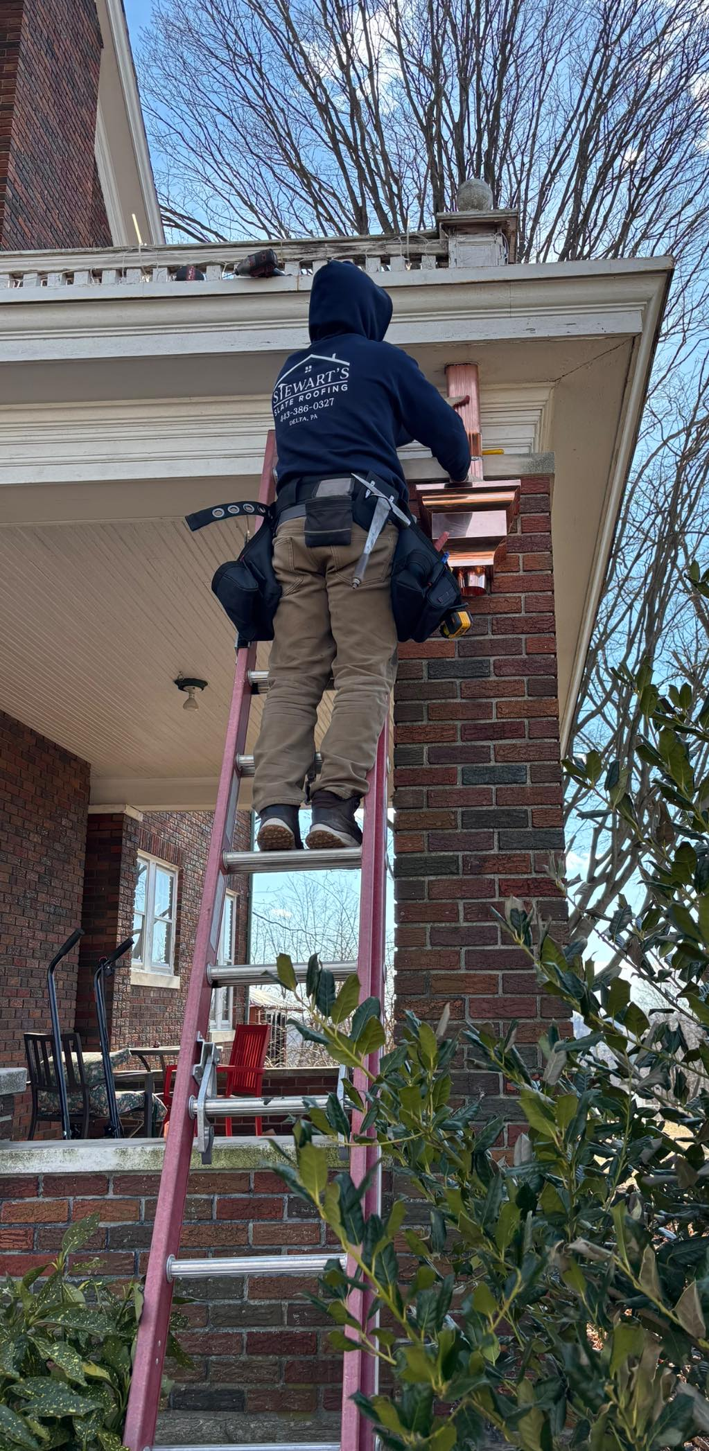 A man is standing on a ladder on the porch of a house.