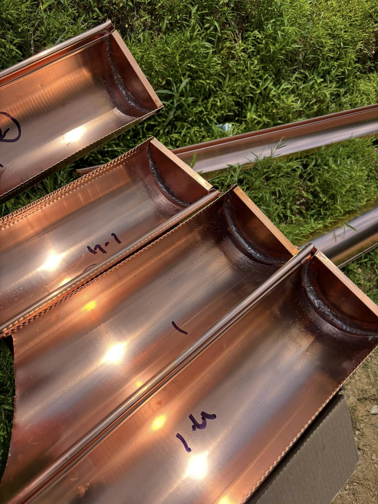Three copper pipes are sitting on top of each other on the grass.