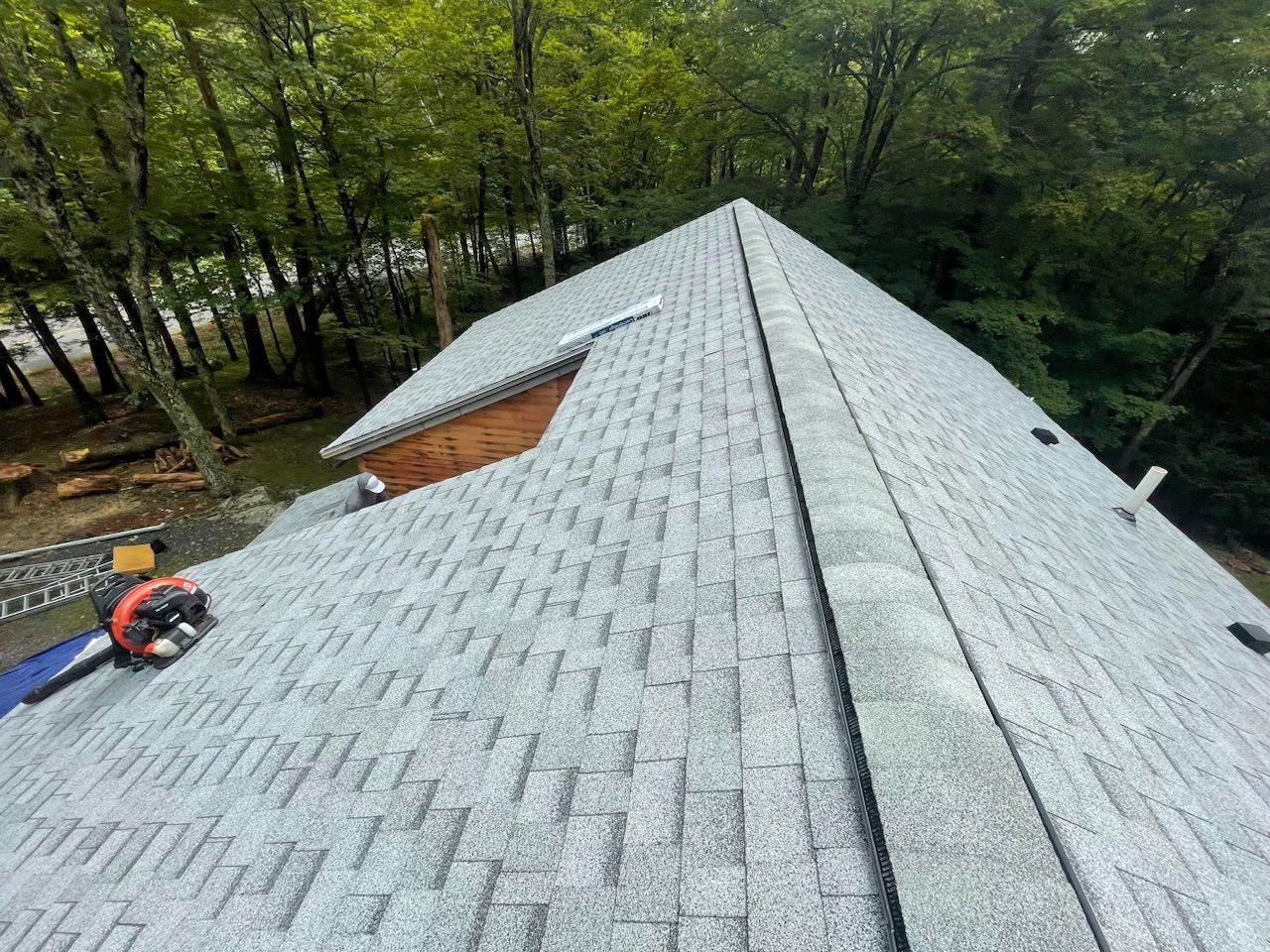Roofing crew working on a gray shingle roof beside a wooded area