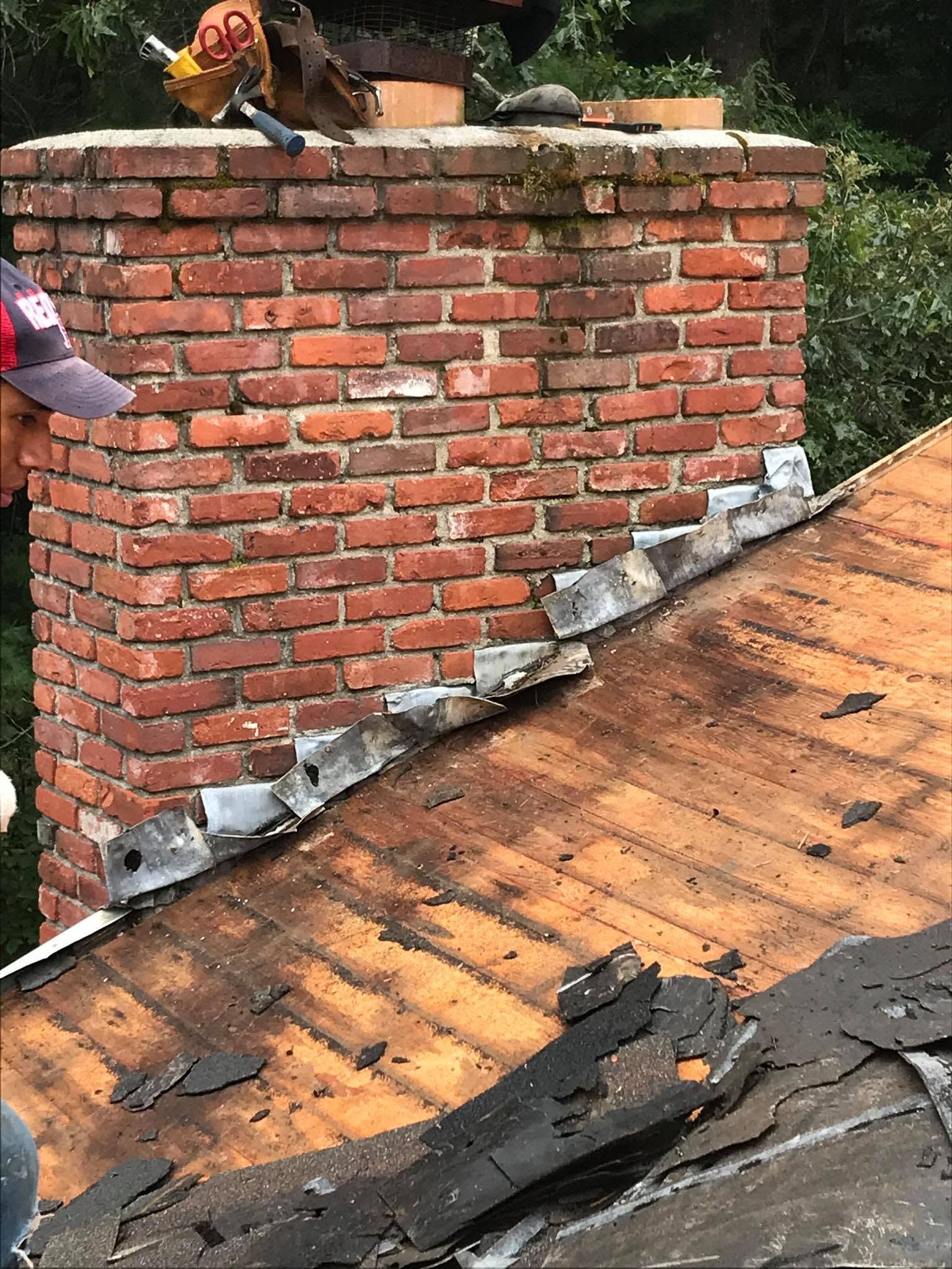 Brick chimney repair on a shingled roof with workers and loose bricks visible