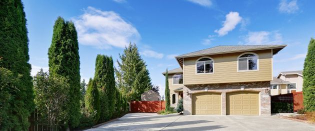 A large house with two garages is surrounded by trees and a driveway.